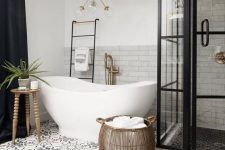 a stylish bathroom with marble and Moroccan tiles, a vintage tub, a shower space with framed glass walls, a gilded chandelier and a basket