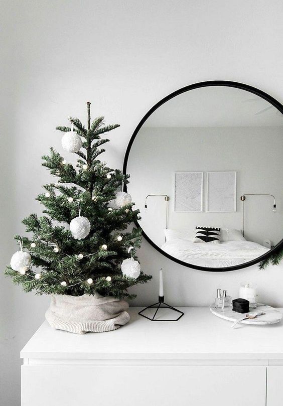 a tabletop Christmas tree with lights and white pompom ornaments is a stylish and minimal idea