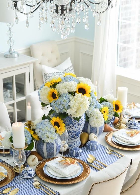 a traditional Thanksgiving table setting with a blue striped tablecloth, blue vases and faux pumpkins looks very stylish