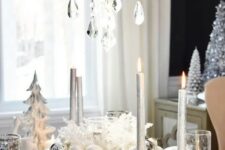 a white and silver table setting with pearly and silver ornaments, a crystal chandelier and patterned glasses