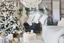 a winter wonderland living room with a flocked Christmas tree with white and gold ornaments, white stockings, mini Christmas trees and fir branches