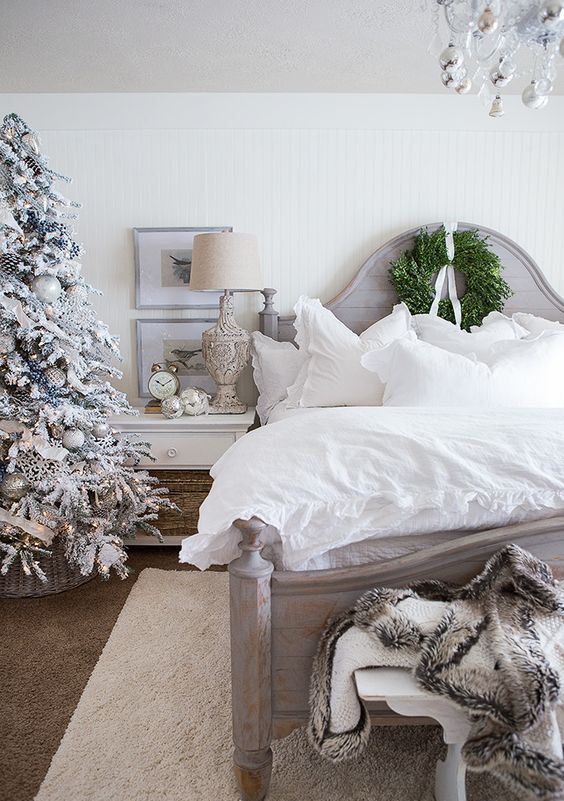 an elegant farmhouse Christmas bedroom with a snowy tree with lights and ornaments, faux fur, a greenery wreath and silver ornaments