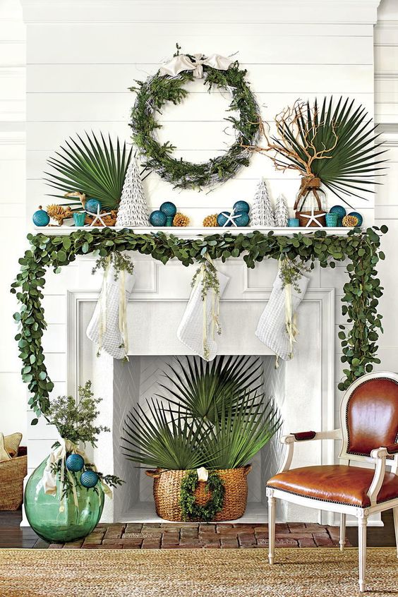 beach Christmas space with a greenery garland and a wreath, tropical leaves, teal Christmas ornaments and mini trees