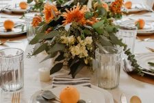 bright fall blooms with greenery and candles paired with bright citrus on the place settings are amazing for a modern Thanksgiving table