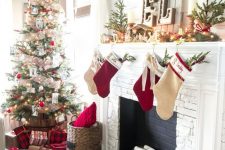 chic rustic Christmas decor with red and neutral stockings, mini trees, fir garland with berries, candles and a Christmas tree with mesh ribbons and white and red ornaments