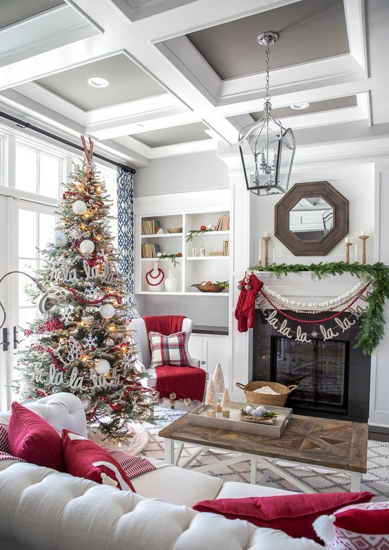 cozy and chic Christmas living room decor with red pillows, bead and pompom garlands, a fir garland, a flocked Christmas tree with lights, snowflakes and letters