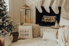 cozy winter holiday decor with white faux fur, white pillows and blankets, a greenery garland, white sotckings and a flocked Christmas tree