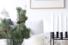 evergreen branches in a large clear vase and a modenr blakc metal candelabra with white candles for a minimal look