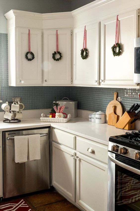 mini evergreen wreaths with red ribbons hanging on cabinets look very cute and make the kitchen feel Christmas