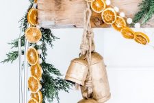 natural Christmas mantel decor with fir branches, dried citrus slices, large vintage bells and pompoms is gorgeous
