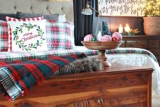 plaid bedding, a snowy evergreen and lights garland, candles, a mini tree in a basket and a bowl with yarn balls and mini trees