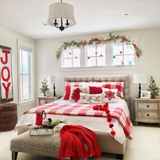 pompom garlands, an evergreen and berry branch, plaid red and white bedding and a red knit blanket for Christmas