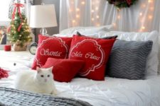 red pillows, an evergreen wreath with a red bow, lights, knit bedding and a mini Christmas tree with a red bow for a festive look
