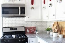 whitewashed bells with plaid ribbons and evergreens mark the cabinets and create a holiday feel in the kitchen
