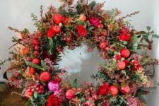 a bold and chic Christmas wreath with greenery and dark foliage, red apples and roses, some moss looks very wild and fresh