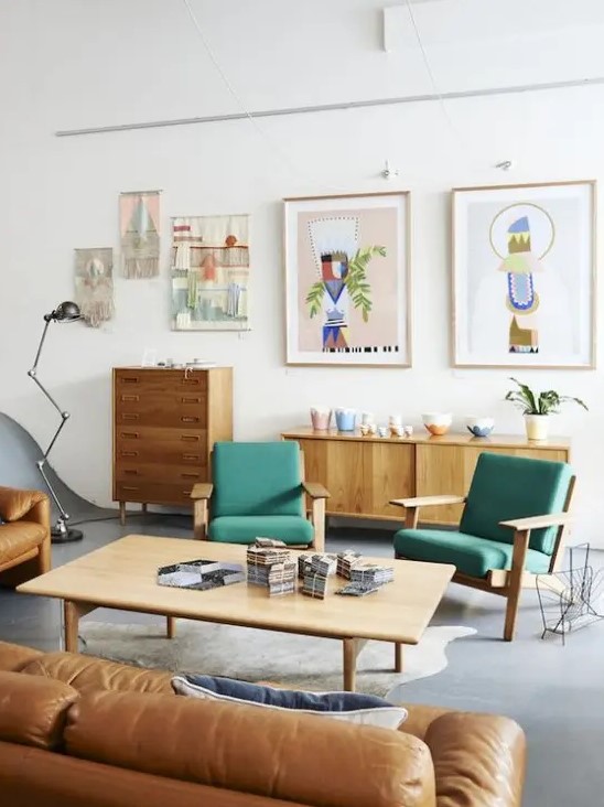 A bright mid century modern living room with stained furniture, green chairs, an amber leather sofa, a low coffee table, a gallery wall and beautiful potted plants