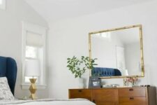 a chic and bright mid-century modern bedroom with white walls, rich stained furniture, a black storage bench and a gilded chandelier