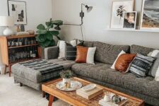 a chic mid-century modern living room with a grey sectional, stained furniture, potted plants, a gallery wall on a ledge is very cozy