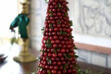 a cone-shaped cranberry Christmas tree with greenery and placed on evergreens is a catchy decoration for the holidays