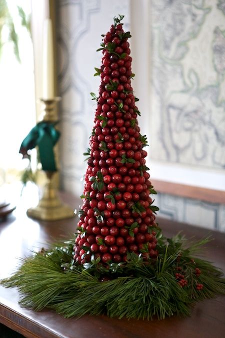 A cone shaped cranberry Christmas tree with greenery and placed on evergreens is a catchy decoration for the holidays