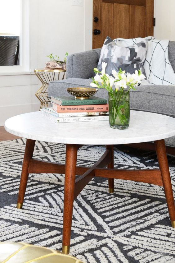 A cool mid century modern coffee table with a white stone tabletop and rich stained legs and a base with gold ends is amazing