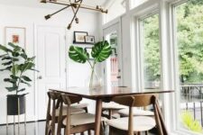 a fresh and light-filled mid-century modern dining space with a stained table, white chairs, a gold chandelier and potted plants
