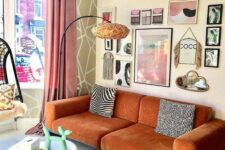 a gorgeous eclectic living room with a modern rust-colored sofa and a matching chair, a round table, a pretty gallery wall and a floor lamp
