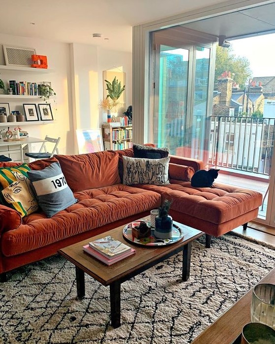 A lovely living room with a rust colored mid century modern sectional, a low table, floating shelves and potted plants here and there