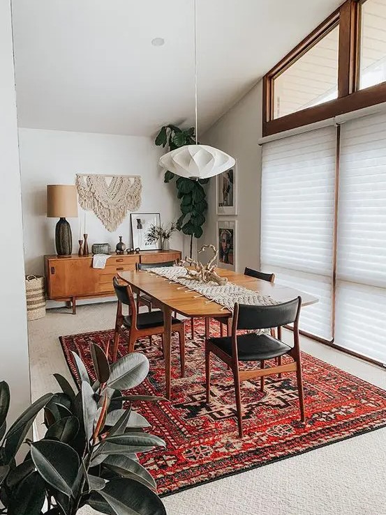 A lovely mid century modern dining room with a credenza, a stained table, black chairs, a faceted pendant lamp and a bold printed rug