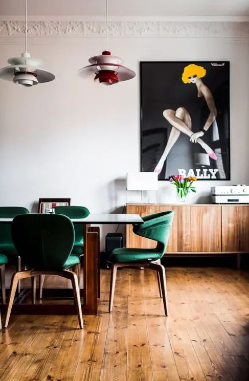 a mid-century modern dining room with emerald chairs, a stained credenza and an oversized poster for a statement