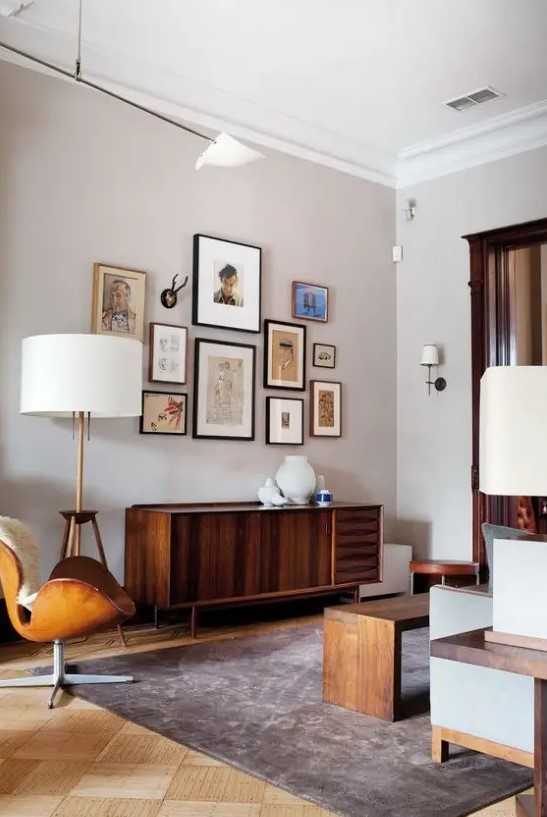 A mid century modern living room done in neutrals, with stained furniture, a leather chair, a credenza, a gallery wall and table lamps