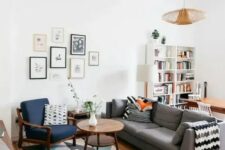 a mid-century modern living room with a bold printed rug, a grey sofa, a navy chair and a white stool, a cool gallery wall