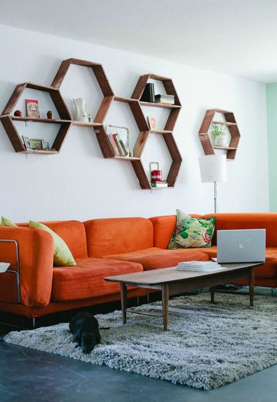 A mid century modern living room with a modern orange sofa, hexagon shelves, a low table and colorful pillows is welcoming