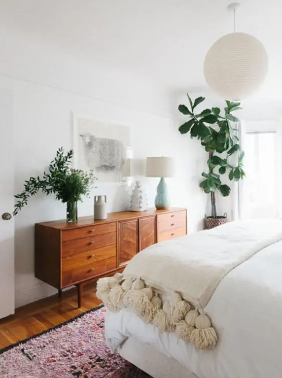 A mid century modern stained dresser is used both for storage and for styling the space, it displays lamps and greenery