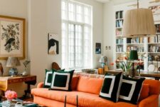 a modern living room with an orange sofa, a pendant lamp, graphic pillows, some coffee tables and lovely artworks