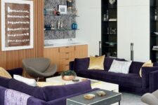 a modern living room with two purple sofas, grey chairs, light stained and black and white storage furniture