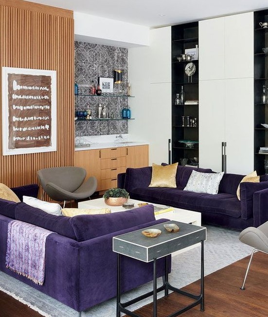 a modern living room with two purple sofas, grey chairs, light stained and black and white storage furniture