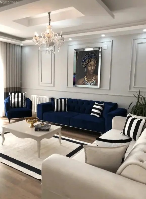 a neutral living room with a modern navy sofa and chair, a creamy sofa, a vintage coffee table and striped pillows and a rug plus a chic crystal chandelier