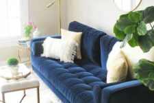 a neutral living room with a modern navy sofa with neutral pillows, a round mirror in a gold frame, a creamy upholstered bench, a gold floor lamp and a side table