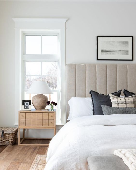 a neutral upholstered bed with an oversized headboard and a catchy wooden nightstand for a chic space