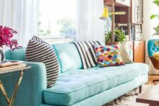 a pretty living room with a modern turquoise sofa, a modern storage unit, a coffee table and touches of gold here and there