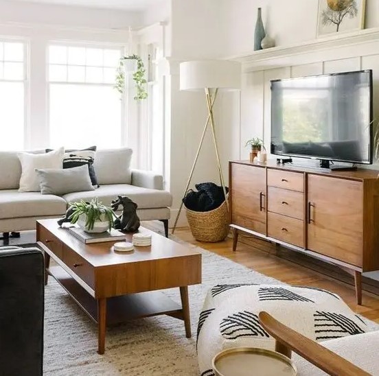 a simple mid-century modern living room with a creamy sofa, a stained TV unit and coffee table, printed pillows and some greenery