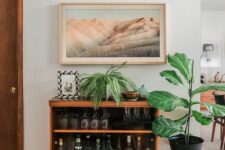 a small mid-century modern cabinet as a home bar, with glasses and bottles and plants around is a cool idea for a modern space