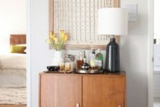 a stained mid-century modern cabinet as a little home bar, with a table lamp wiht a black base an an artwork over it