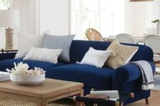 a stylish and contrasting nautical living room with a modern navy sofa, neutral pillows, a wooden coffee table and a folding chair, a wicker pendant lamp