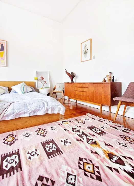 A welcoming and bright mid century modern space with warm stained wooden furniture, a pink rug and some artworks
