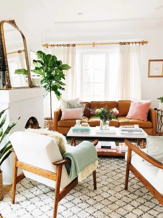 a welcoming mid-century modern lviing room with a non-working fireplace, an amber leather sofa, white chairs, a low coffee table, a mirror and pastel pillows