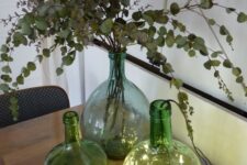 an arrangement of green bottles with lights, with dried eucalyptus is a cool decoration idea for your space