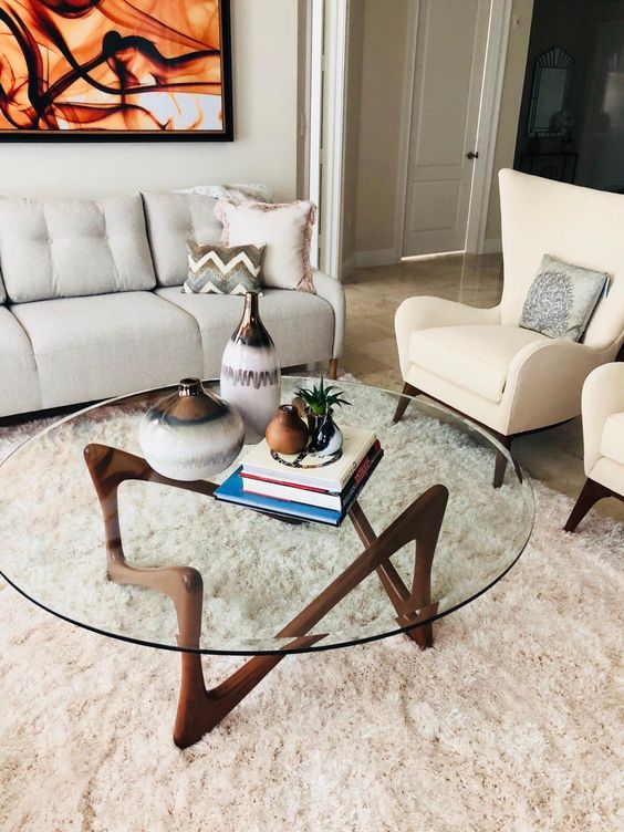 An eye catchy mid century modern coffee table with a round clear glass tabletop and a quirky dark stained wooden base is wow