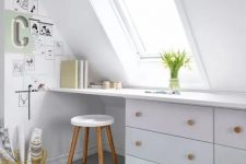 a Nordic attic home office in white, with a skylight, a built-in desk, a stool and a small gallery wall plus blooms
